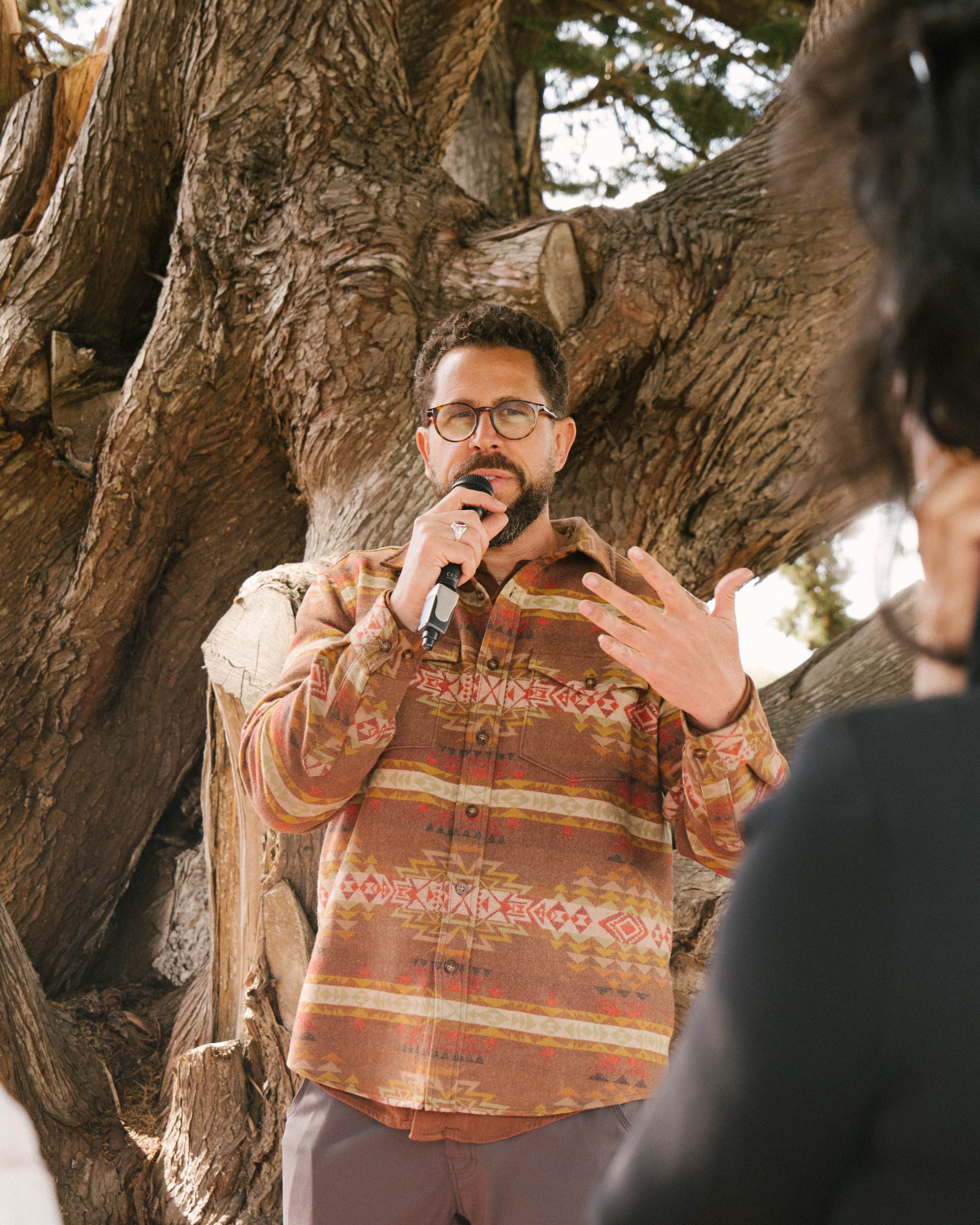 Dr. Abdallah Rothman speaking to a group outdoors beneath a large tree